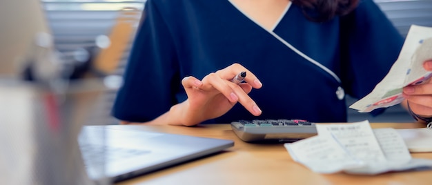 Foto imprensa de mão de mulher de close-up na calculadora e cálculo mensal de contas de dívida, escrevendo fazer relatório para planejar as despesas no futuro na mesa no escritório em casa.