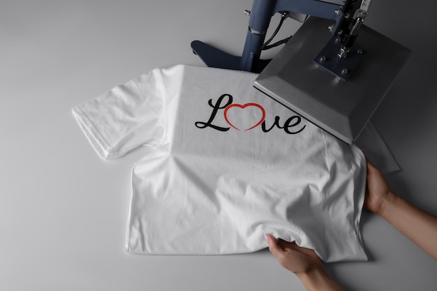 Impresión de logotipo Mujer con camiseta usando prensa térmica en la mesa blanca por encima de la vista