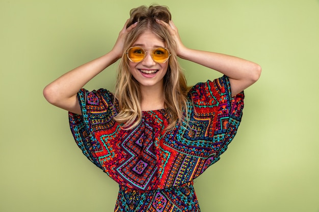 Impresionada joven rubia eslava con gafas de sol poniendo las manos sobre su cabeza y