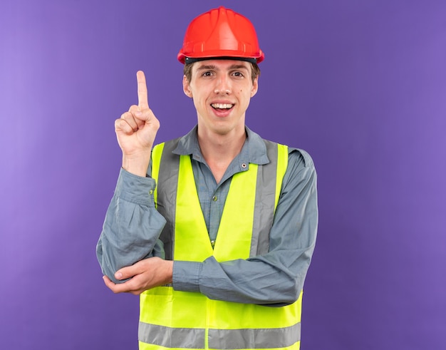 Foto impresionado joven constructor en puntos uniformes en arriba aislado en la pared azul