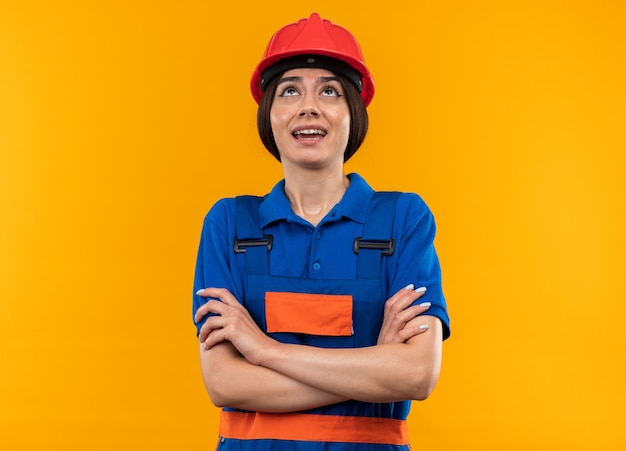 Impresionado mirando hacia arriba a mujer joven constructora en uniforme cruzando las manos