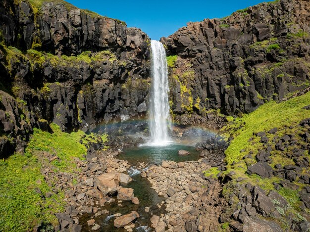 Impresionante cascada de Islandia con agua helada y la piscina en la base llena de rocas en un soleado