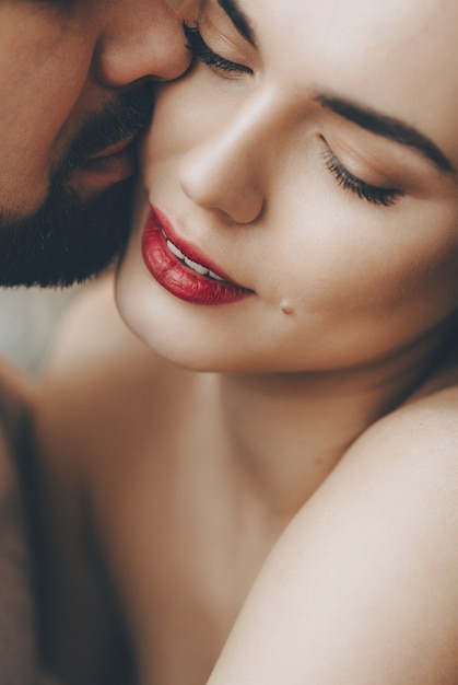 Impresionante chica caucásica con labios rojos es besada por su amante barbudo mientras se abrazan