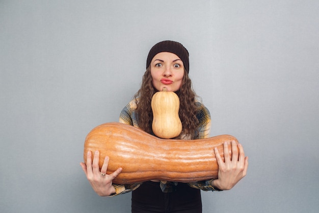 Impresionante chica sosteniendo calabazas grandes y pequeñas sobre un fondo gris.