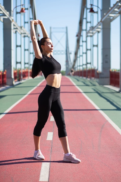 Impresionante deporte mujer haciendo estiramientos antes de correr en el puente