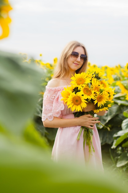 Impresionante foto, hermosa joven rubia de pie entre los girasoles