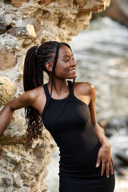 Impresionante joven afro en vestido negro de verano posando en las ruinas del bosque