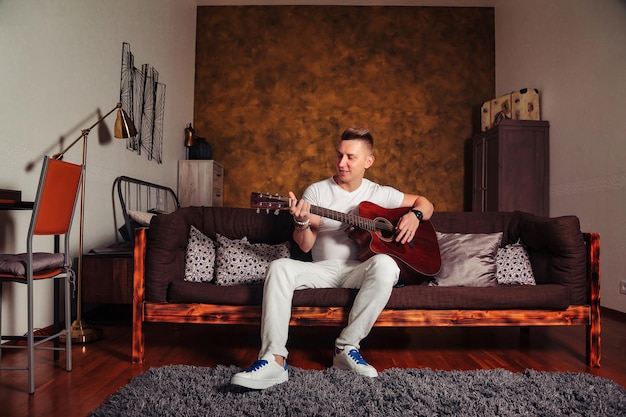 Impresionante joven vestido de blanco con guitarra en la habitación interior