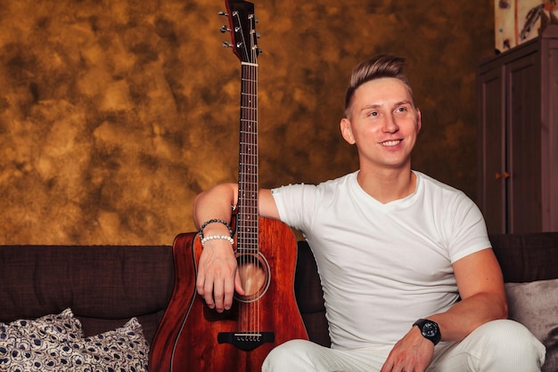 Impresionante joven vestido de blanco con guitarra en la habitación interior