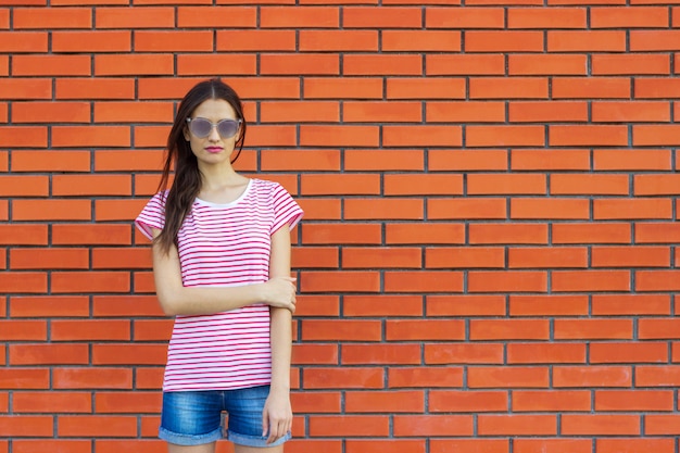 Impresionante mujer joven posando al aire libre sobre pared de ladrillo