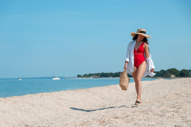 Impresionante mujer joven en traje de baño rojo caminando por la playa de mar traje de verano