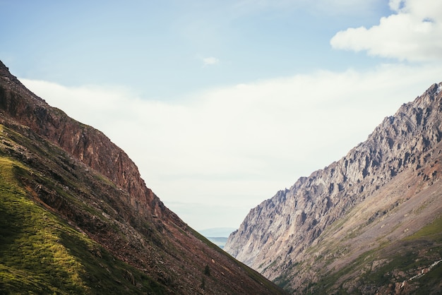 Impresionante paisaje alpino simétrico minimalista con dos grandes montañas diagonales con rocas bajo un cielo nublado azul. Pintoresco paisaje de montaña mínima soleada con simetría de dos altas montañas a la luz del sol.