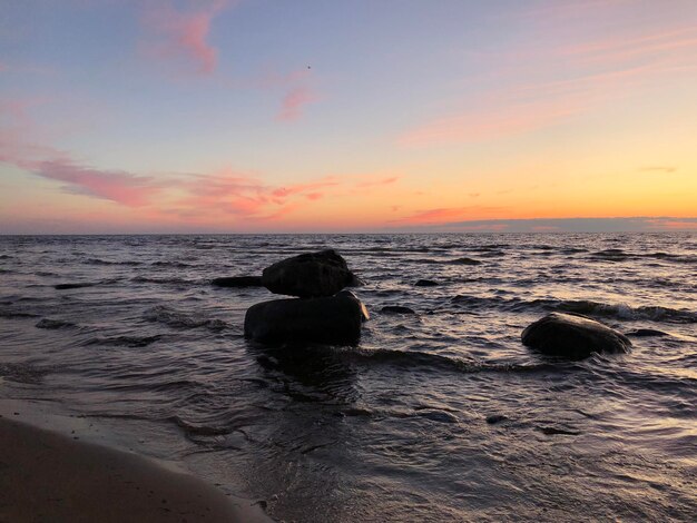 Impresionante paisaje marítimo con puesta de sol cielo aguas onduladas gran piedra azul naranja rosa amarillo cielo playa vacía