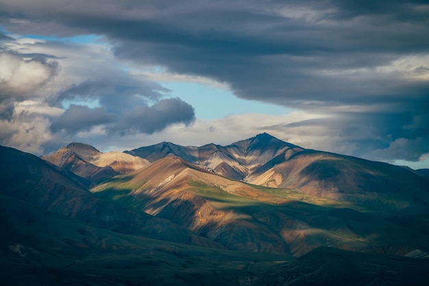 Impresionante paisaje montañoso con grandes montañas y espacio azul en el cielo nublado en un clima nublado. tragaluz azul en el cielo nublado sobre enormes montañas multicolores en la luz del sol. paisaje de montaña colorido