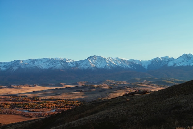 Impresionante paisaje otoñal con multitud de turistas en la colina con vistas al valle rojo y la gran cordillera cubierta de nieve en el sol rojo del atardecer. Espectacular vista soleada a las montañas nevadas y al valle otoñal.