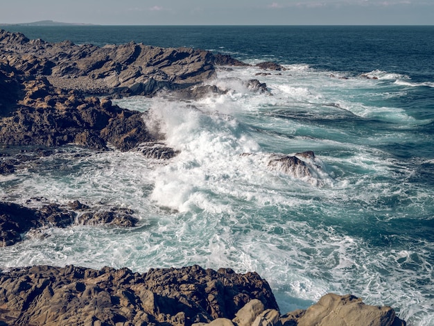 Impresionante paisaje de poderoso mar azul espumoso que baña la costa rocosa durante el día