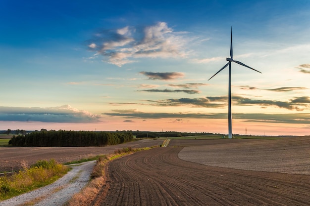 Impresionante puesta de sol en el campo marrón con turbina eólica en otoño