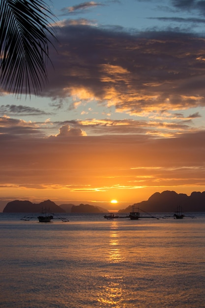 Impresionante puesta de sol en la playa tropical Cielo brillante de la tarde en la laguna con siluetas de barcos e isla