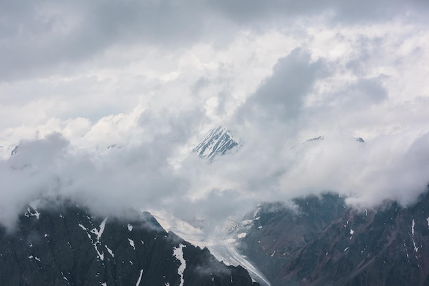 Impresionante vista aérea de la cima de la montaña nevada y la larga lengua del glaciar en densas nubes bajas Paisaje mínimo de montaña con un hermoso pico y un gran glaciar en nubes espesas Minimalismo de montaña en la nube