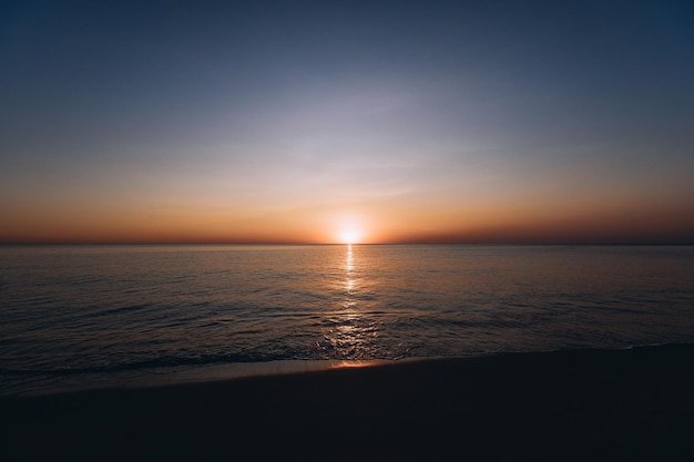 Impresionante vista del atardecer de verano en la playa. Maravilloso paisaje al atardecer en el mar profundo y oscuro y el cielo anaranjado sobre él y las olas tranquilas fluyen sobre él.