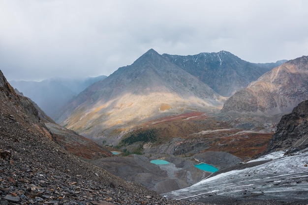 Impresionante vista desde la cima de los lagos de ojos turquesa y la alta montaña en forma de pirámide tres hermosos lagos de montaña entre los colores desvanecidos del otoño pequeños lagos glaciares y picos afilados luz del sol y sombras de nubes