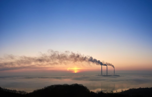 Impresionante vista del colorido cielo azul y rosa con un brillante sol naciente en la central termoeléctrica. Chimeneas térmicas que producen humo denso con gases tóxicos a la atmósfera. Concepto de generación de energía.