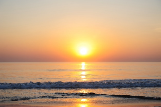 Impresionante vista del mar en los rayos del sol poniente, la luz del sol rojizo se refleja en el agua. Hermosa puesta de sol sobre el océano, playa desierta, espacio de copia