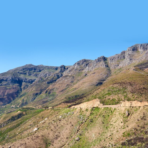 Impresionantes montañas verdes con un fondo de cielo azul y espacio de copia Rocas en una montaña salvaje con hermosas texturas ásperas naturales en verano Paisaje natural al aire libre de plantas arbustivas en colinas onduladas