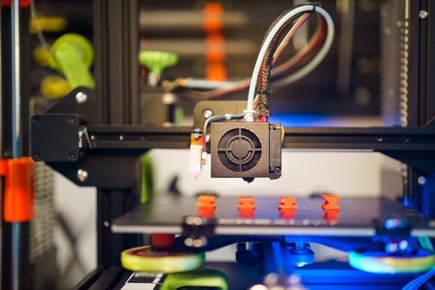 Impresora 3D con piezas naranjas impresas Fondo de laboratorio doméstico