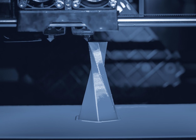 Impresora 3D que imprime volumen aislado objeto triangular color gris azul sobre la base de fondo azul y negro primer plano Tecnología de impresión 3d moderna Tecnología aditiva moderna progresiva