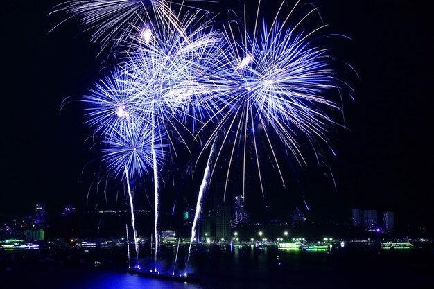 Impressionantes fogos de artifício azuis e brancos explodindo no céu noturno sobre a baía
