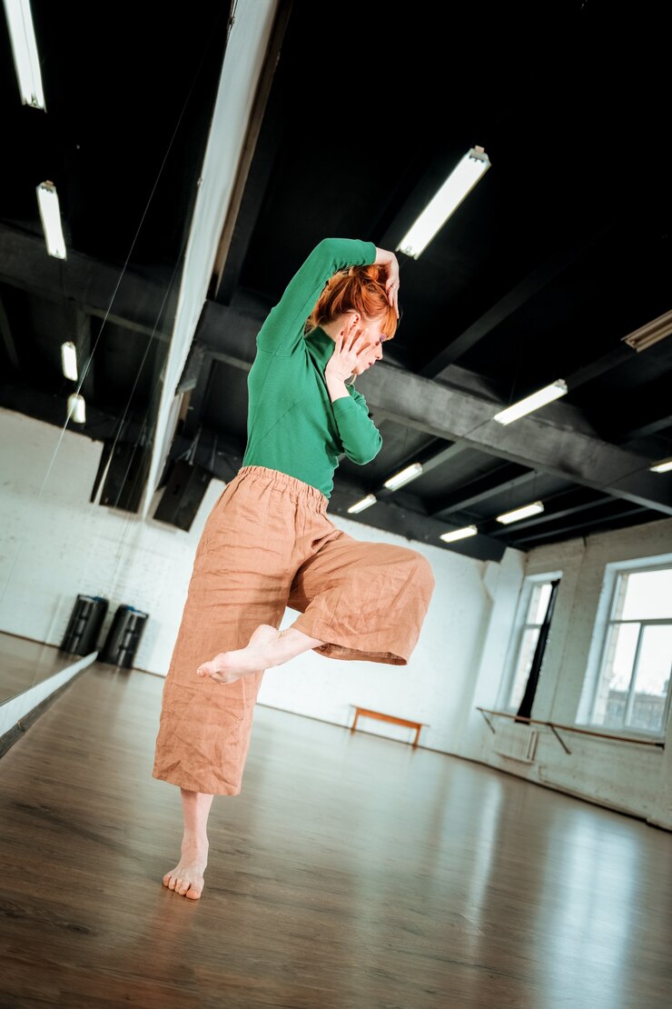 Foto improvisação. professora de dança profissional ruiva em pé sobre uma perna enquanto dança no estúdio