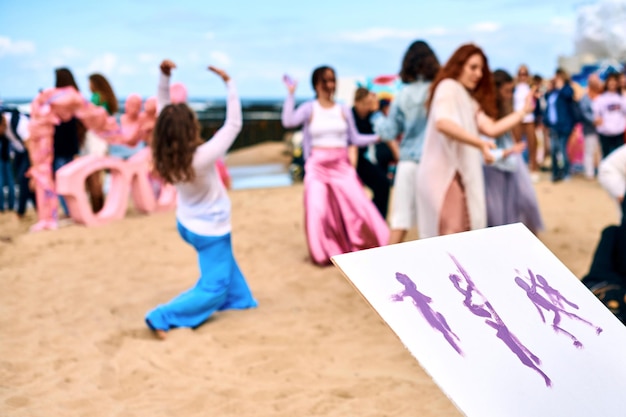 Improvisationszeichnung Kunstperformance im Freien mit tanzenden Mädchen am Sandstrand Maler Künstlerzeichnung auf weißer Leinwand Improvisationsbild Kreatives Kunstfestival am Meeresstrand