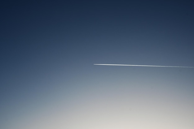 In den blauen Himmel eine weiße Spur von einem fliegenden Flugzeug Hintergrund des blauen Himmels