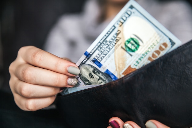 In den Händen der Frauen liegt die braune Lederbrieftasche mit einem Bündel von hundert Dollar. Geschäftsvorschlag. Schöne Maniküre