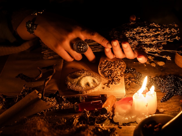 In den Händen der Hexen Bündel trockener Kräuter zur Weissagung. Das Licht der Kerzen auf dem alten Zaubertisch. Attribute von Okkultismus und Magie.