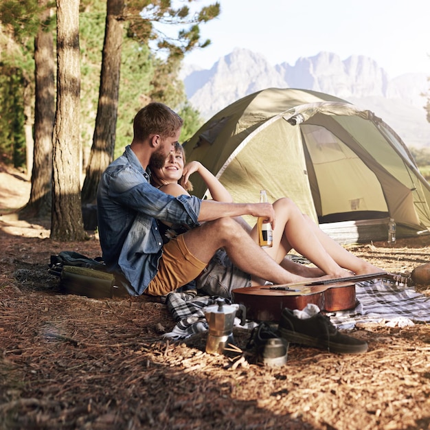 In den Wald Aufnahme eines liebevollen jungen Paares, das auf seinem Campingplatz sitzt