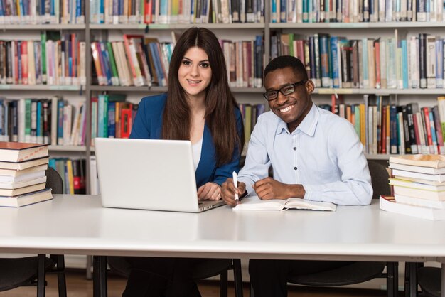 In der Bibliothek Hübsche zwei College-Studenten mit Laptop und Büchern, die in einer High School-Universitätsbibliothek arbeiten. Geringe Schärfentiefe