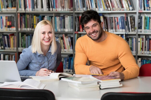 In der Bibliothek Hübsche zwei College-Studenten mit Laptop und Büchern, die in einer Universitätsbibliothek einer High School arbeiten