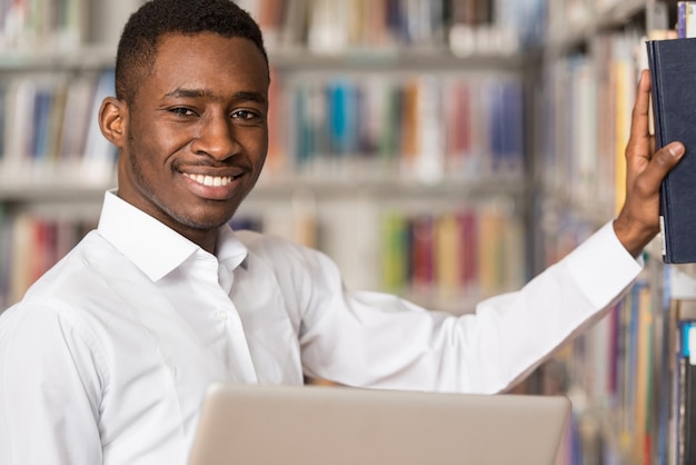 In der Bibliothek Hübscher männlicher Student mit Laptop und Büchern, die in einer High School-Universitätsbibliothek arbeiten Geringe Schärfentiefe