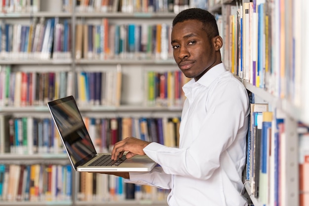 In der Bibliothek Hübscher männlicher Student mit Laptop und Büchern, die in einer High School-Universitätsbibliothek arbeiten Geringe Schärfentiefe