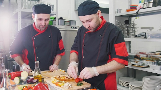 In der Küche arbeiten zwei Männer, die den Fisch mit Gemüse füllen