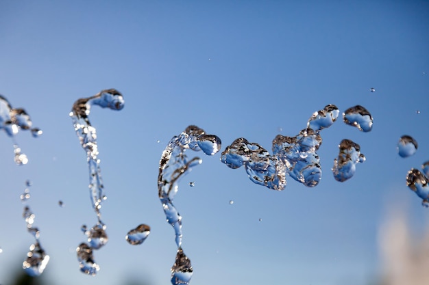 Foto in der luft gefrorene wassertröpfchen mit spritzern und kettenblasen auf einem blauen, isolierten hintergrund in der natur. klare und transparente flüssigkeit, die gesundheit und natur symbolisiert