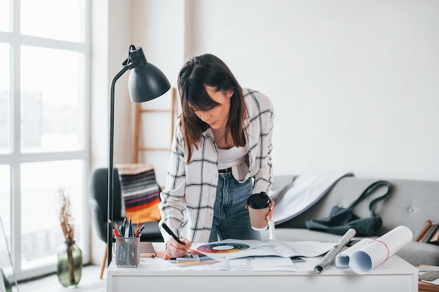 In der Nähe des Tisches stehend Junge freiberufliche Arbeitnehmerin ist tagsüber zu Hause