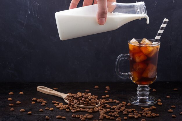 In ein Glas kalten Kaffee goss Milch aus einer Flasche