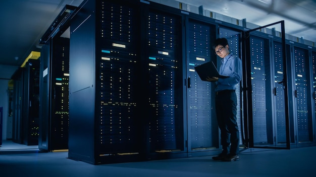 In einem Datenzentrum IT-Techniker Mann Wartungsprogramm auf einem Laptop ausführen Steuerung Betriebs-Server-Rack Optimales Funktionieren Moderne Hightech-Telekommunikationsbetriebs-Supercomputer