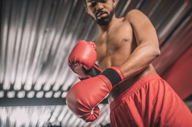 In einem Fitnessstudio. Dunkelhäutiger Kickboxer in roten Shorts und roten Boxhandschuhen