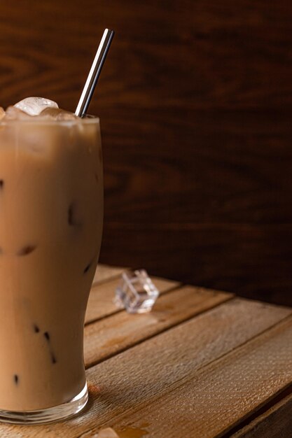 In einem Glas bis zum Rand gefüllt mit Eis und Kaffee mit Milch. Ein Glas Eiskaffee steht auf einer Kiste vor einem dunklen Holzhintergrund.