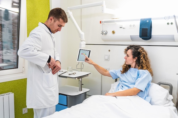 In einem Krankenzimmer zeigt ein im Bett sitzender Patient einem aufmerksamen Arzt eine Umfrage auf einem Tablet