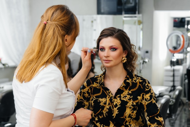 In einem schönen, modernen Schönheitssalon macht ein professioneller Make-up-Stylist Make-up für ein junges Mädchen. Schönheit und Mode.